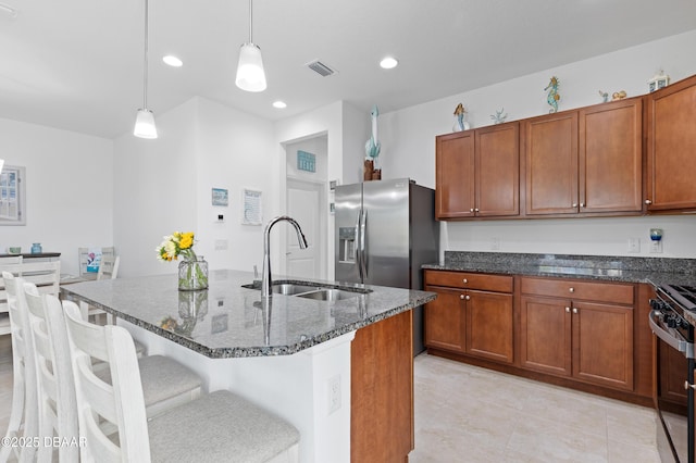 kitchen with visible vents, brown cabinets, a sink, dark stone countertops, and stainless steel appliances