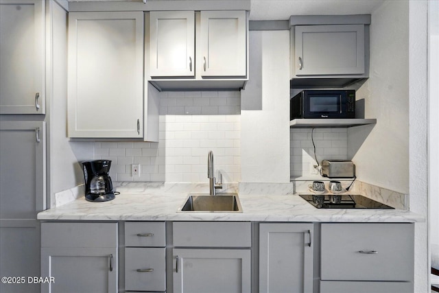 kitchen with gray cabinetry, a sink, black appliances, and backsplash