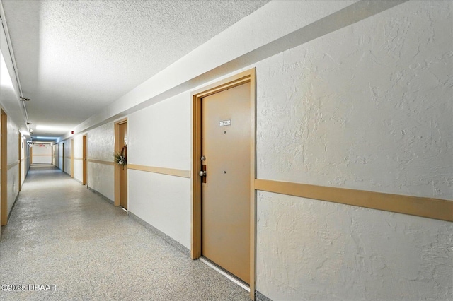corridor featuring a textured wall, a textured ceiling, and dark aggregate flooring