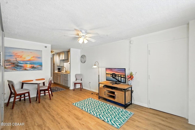 living room featuring light wood-style flooring, ceiling fan, a textured ceiling, and baseboards