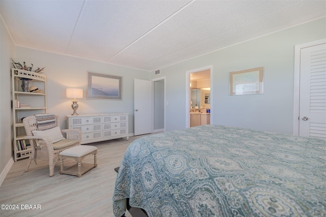 bedroom with light wood-type flooring, a textured ceiling, and ensuite bath