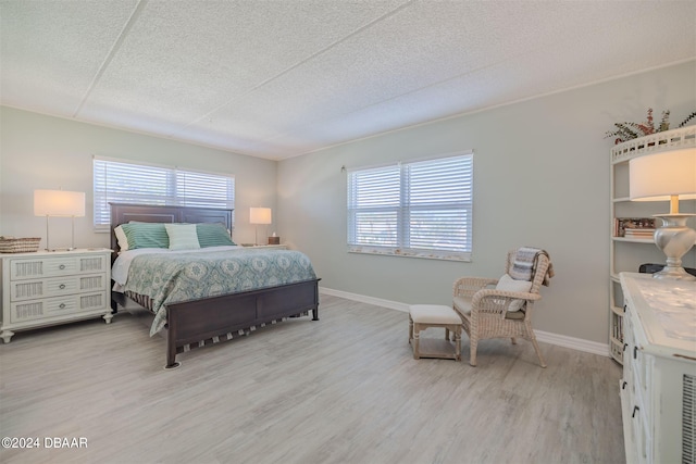 bedroom featuring a textured ceiling, light hardwood / wood-style flooring, and multiple windows