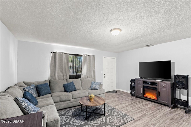 living area with light wood finished floors, baseboards, visible vents, and a textured ceiling