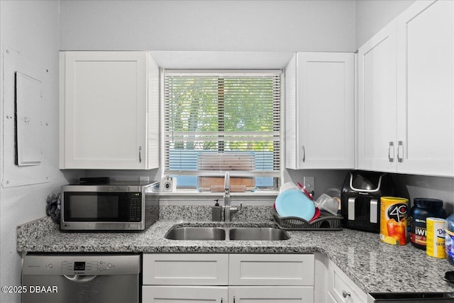 kitchen with white cabinets, light stone countertops, stainless steel appliances, and a sink