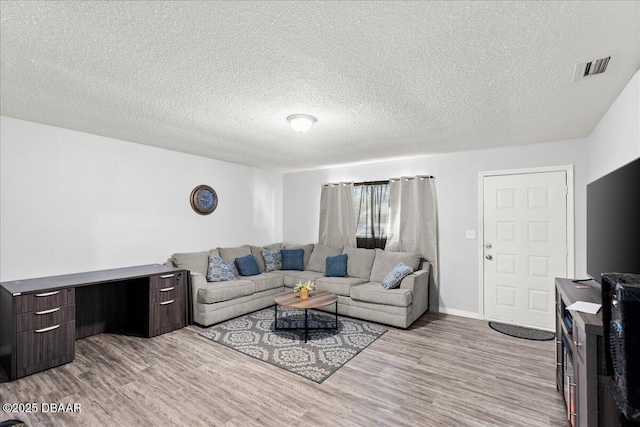 living area featuring baseboards, light wood-style flooring, visible vents, and a textured ceiling