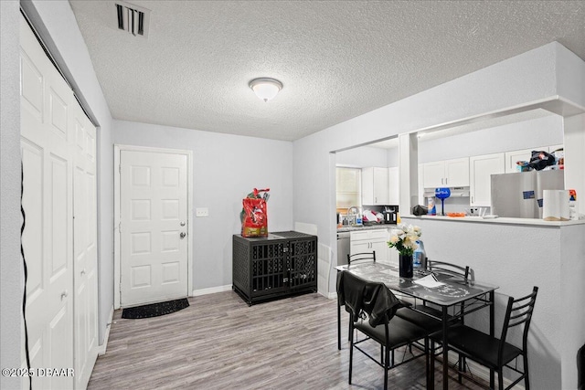 dining space with a textured ceiling, light wood finished floors, visible vents, and baseboards