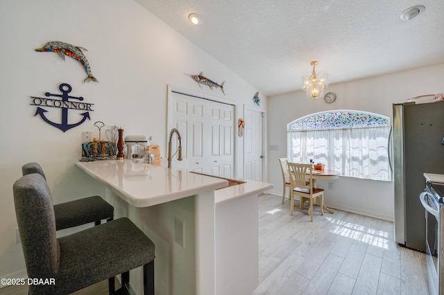 49 Felshire Ln, Palm Coast, FL 32137 - kitchen featuring a peninsula, a kitchen breakfast bar, a chandelier, freestanding refrigerator, and a textured ceiling