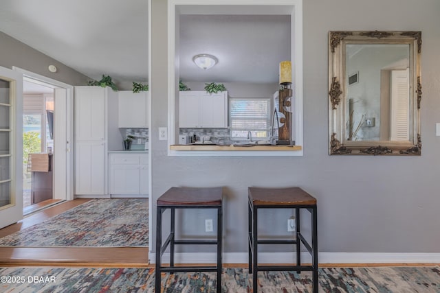 kitchen featuring visible vents, backsplash, white cabinets, wood finished floors, and baseboards