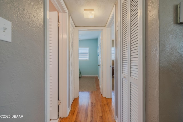 hallway featuring light wood-style flooring, baseboards, and a textured wall