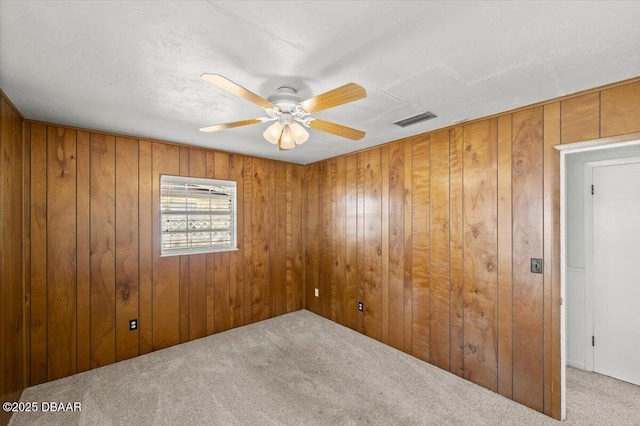 carpeted spare room featuring ceiling fan and wood walls