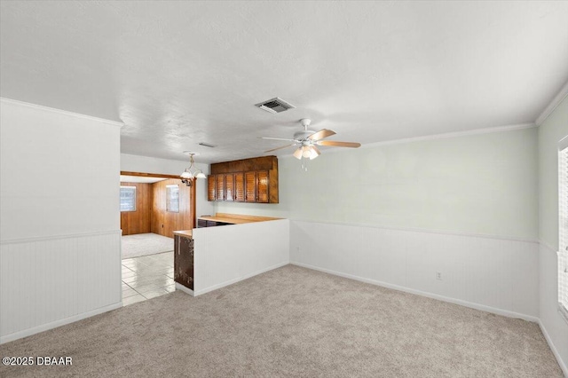 unfurnished living room featuring ornamental molding, ceiling fan with notable chandelier, light carpet, and a textured ceiling