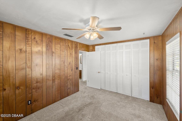 unfurnished bedroom with multiple windows, wooden walls, light colored carpet, and ceiling fan