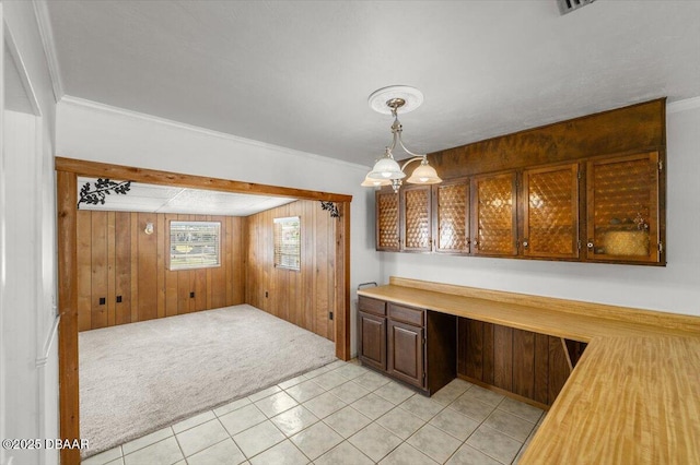 kitchen featuring wood walls, built in desk, ornamental molding, pendant lighting, and light colored carpet