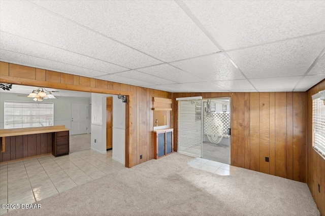 interior space with a drop ceiling, light colored carpet, and wood walls