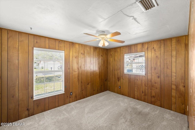 empty room with ceiling fan, carpet flooring, a textured ceiling, and wood walls