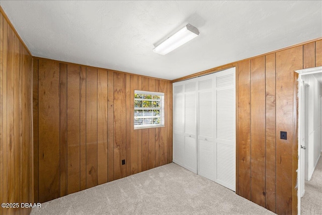 unfurnished bedroom with wooden walls, light colored carpet, and a closet