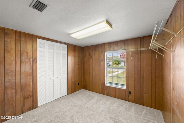 unfurnished bedroom featuring a textured ceiling, carpet, and wood walls