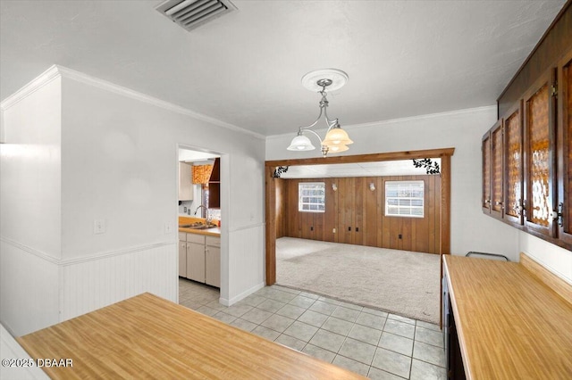 unfurnished dining area with sink, an inviting chandelier, crown molding, light tile patterned floors, and wooden walls