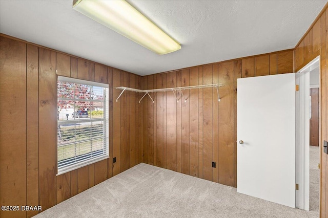 empty room with carpet, a textured ceiling, and wood walls