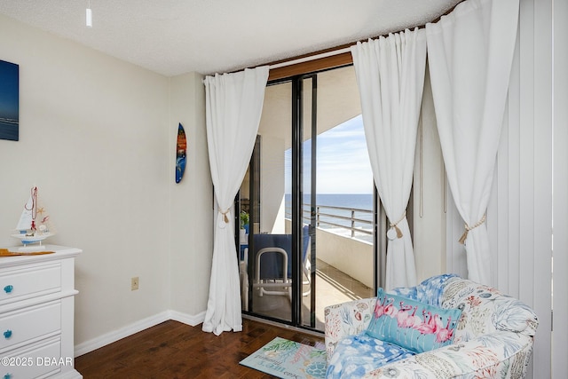 interior space featuring wood finished floors, baseboards, access to exterior, a water view, and a textured ceiling