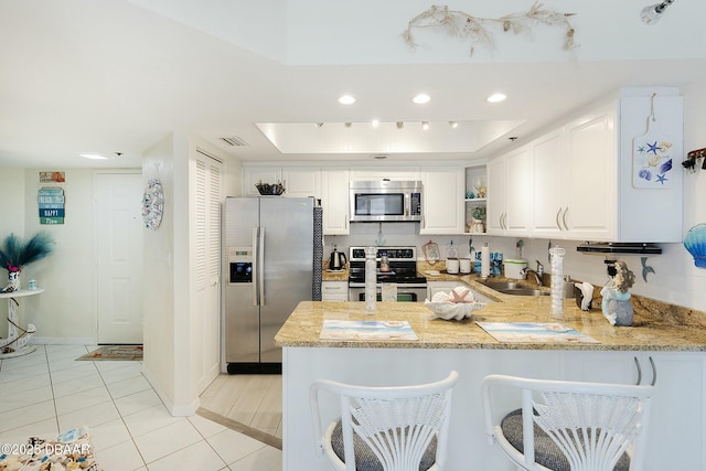 kitchen with visible vents, a tray ceiling, a peninsula, stainless steel appliances, and a sink