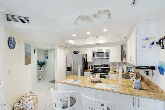 kitchen with visible vents, a tray ceiling, appliances with stainless steel finishes, a peninsula, and light stone countertops