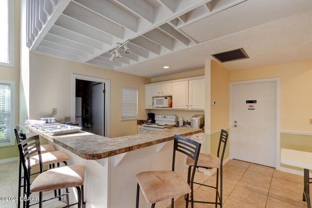 118 Lagoon Ct, New Smyrna Beach, FL 32169 - kitchen featuring light tile patterned floors, a kitchen bar, white cabinetry, visible vents, and white appliances