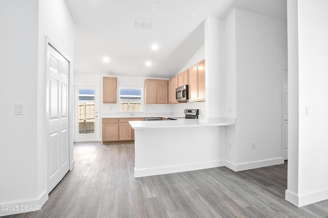 kitchen featuring kitchen peninsula, light brown cabinetry, stainless steel appliances, light hardwood / wood-style floors, and lofted ceiling