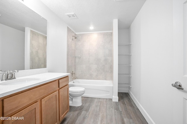 full bathroom featuring vanity, hardwood / wood-style flooring, tiled shower / bath combo, toilet, and a textured ceiling