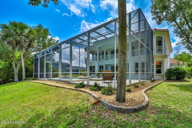 back of house with a balcony, a lawn, glass enclosure, and a patio area