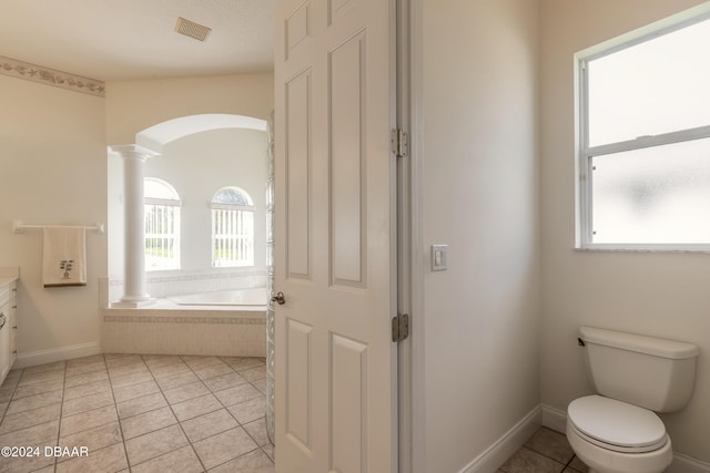 bathroom featuring tiled bath, tile patterned floors, vanity, toilet, and decorative columns