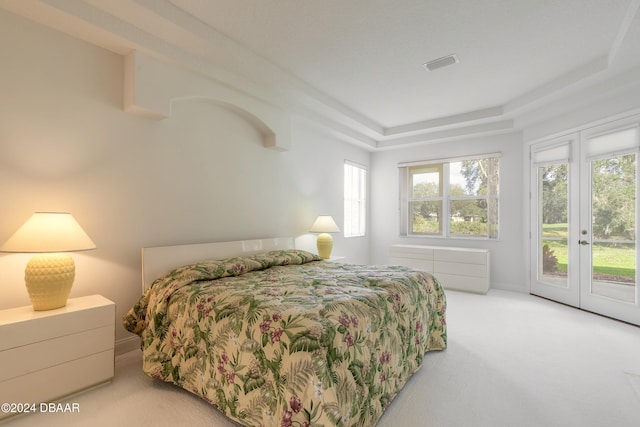 bedroom with access to outside, a tray ceiling, and light carpet