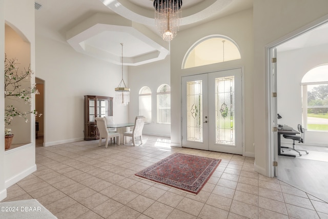 tiled entrance foyer with a towering ceiling, a raised ceiling, and french doors