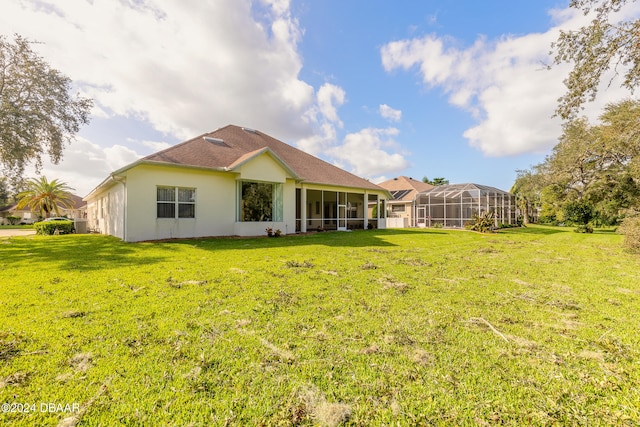 rear view of property with glass enclosure, a lawn, and a sunroom