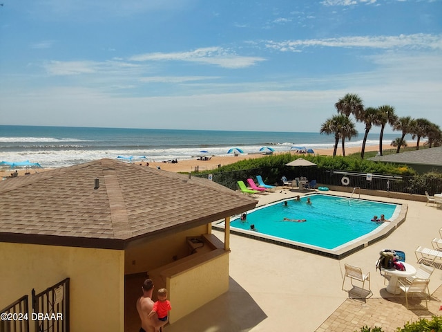 view of pool featuring a water view, a patio, and a beach view