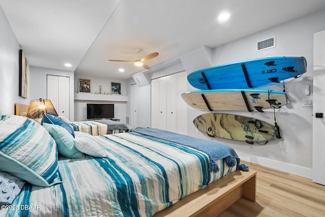 bedroom featuring ceiling fan, light hardwood / wood-style flooring, and multiple closets