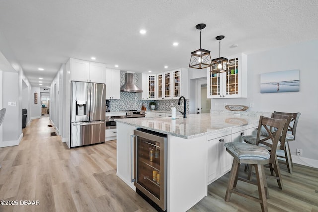 kitchen with wall chimney range hood, stainless steel appliances, wine cooler, hanging light fixtures, and kitchen peninsula