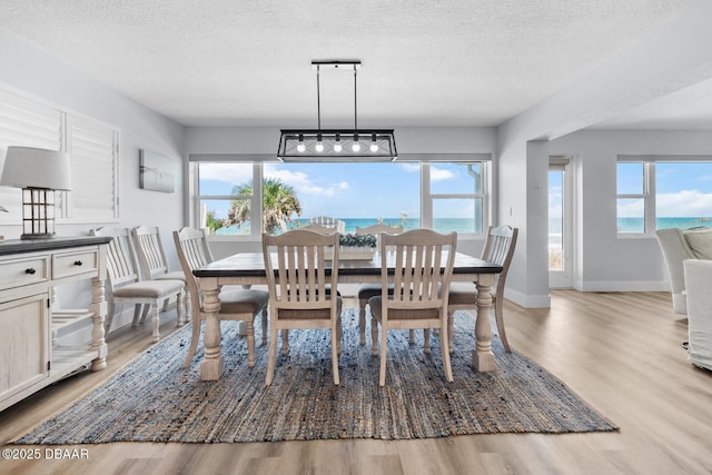 dining area featuring a textured ceiling, a water view, and light wood-type flooring