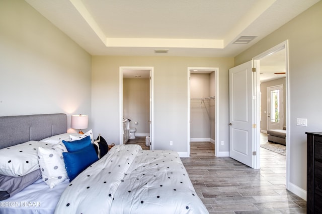 bedroom featuring connected bathroom, a spacious closet, a raised ceiling, a closet, and light hardwood / wood-style floors