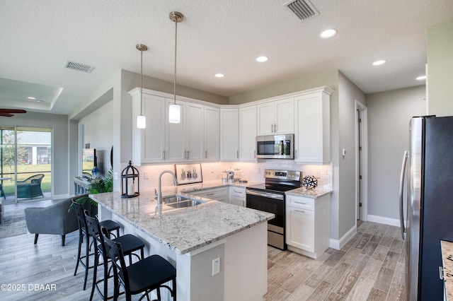 kitchen with stainless steel appliances, decorative light fixtures, kitchen peninsula, and white cabinets