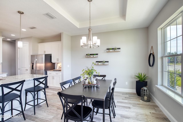 dining area featuring a raised ceiling, light hardwood / wood-style flooring, and a notable chandelier