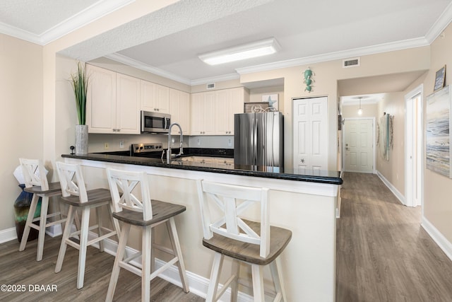 kitchen featuring appliances with stainless steel finishes, a breakfast bar, a textured ceiling, white cabinets, and light hardwood / wood-style floors