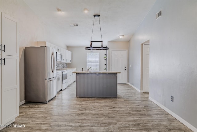 kitchen with hanging light fixtures, light wood-type flooring, appliances with stainless steel finishes, a kitchen island, and white cabinets