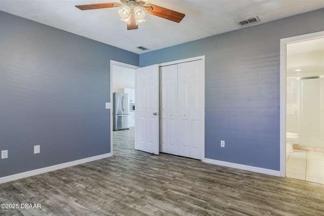 unfurnished bedroom with connected bathroom, hardwood / wood-style floors, stainless steel fridge, ceiling fan, and a closet