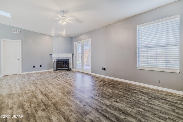 unfurnished living room featuring a tile fireplace, wood-type flooring, ceiling fan, and french doors