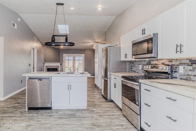 kitchen featuring appliances with stainless steel finishes, hanging light fixtures, a center island with sink, and white cabinets