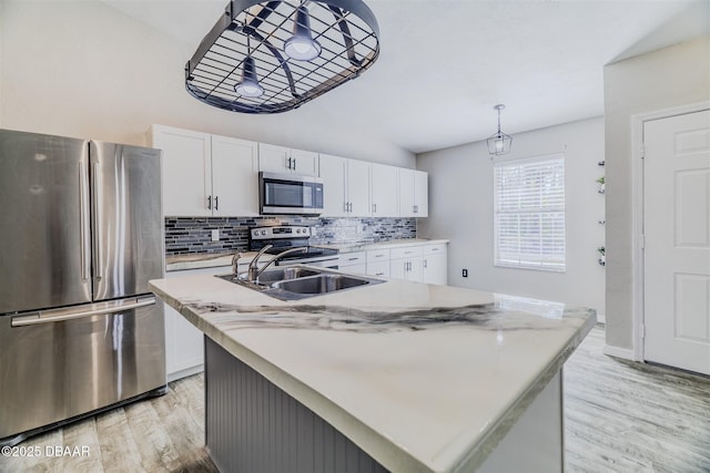 kitchen featuring stainless steel appliances, tasteful backsplash, white cabinets, a center island with sink, and light wood-type flooring