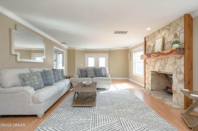 living room featuring french doors, ornamental molding, a stone fireplace, and light hardwood / wood-style flooring