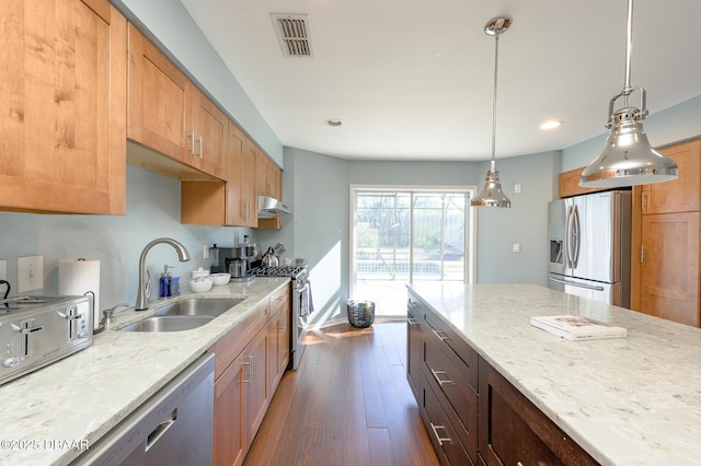 kitchen featuring sink, hanging light fixtures, appliances with stainless steel finishes, dark hardwood / wood-style flooring, and light stone countertops