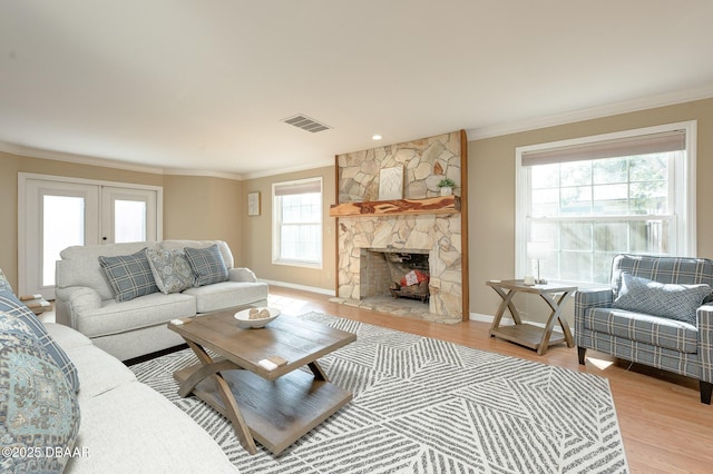 living room with french doors, a stone fireplace, light hardwood / wood-style floors, and a wealth of natural light